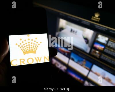 Personne détenant un téléphone portable avec le logo de la société australienne Crown Resorts Limited à l'écran devant la page Web. Mise au point sur l'affichage du téléphone. Banque D'Images