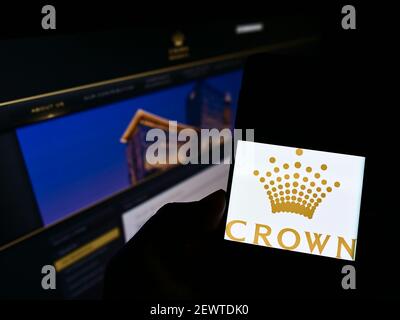 Personne détenant un smartphone avec le logo de la société australienne Crown Resorts Limited à l'écran devant le site Web. Mise au point sur l'affichage du téléphone. Banque D'Images