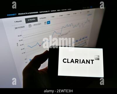 Personne tenant un téléphone portable avec logo de la société suisse de produits chimiques spécialisés Clariant AG sur écran devant le site web avec carte. Mise au point sur l'affichage du téléphone. Banque D'Images