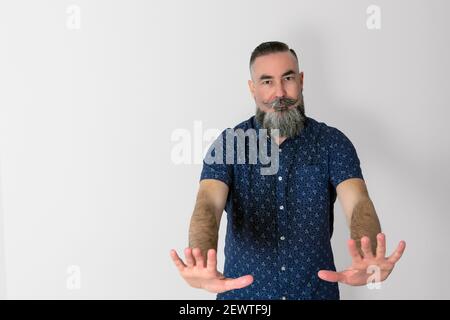 Hipster caucasien de 40-45 ans avec une grande barbe grise, avec un visage sérieux et les mains en avant dans un signe clair de l'ordre de l'arrêter. Banque D'Images