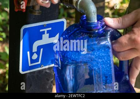 Le 22 août 2021 - Bolton, QC, Canada : remplissage de l'eau potable dans une bouteille réutilisable au point d'eau potable d'un terrain de camping, les mains de l'homme portant un contenant Banque D'Images