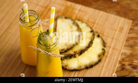 Jus d'ananas frais avec glace dans un petit verre bouteille sur fond de bois Banque D'Images