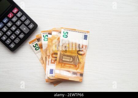 Billets en euros et calculatrice sur table blanche Banque D'Images