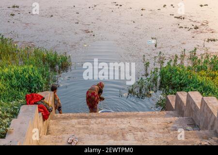 Femme rurale lavant ses vêtements sur une rive de rivière tandis que son enfant regarde un village du Bengale occidental, en Inde Banque D'Images