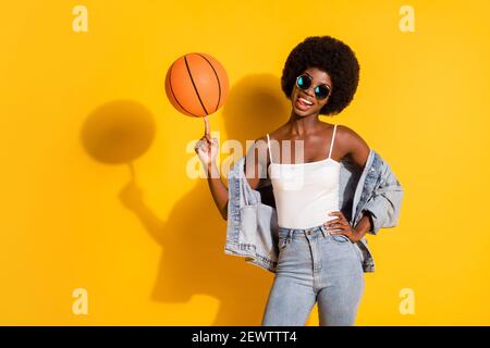 Photo de jeune fille sportive et sexy tenue décontractée en denim basket-ball tournant montrant un arrière-plan jaune isolé de la langue Banque D'Images