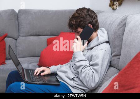un jeune homme parle au téléphone et travaille sur l'ordinateur portable. soyez à la maison en période de pandémie Banque D'Images