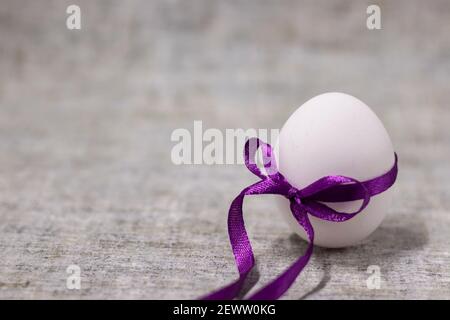 œuf de poulet emballé dans un nœud papillon violet. nourriture saine et crue. œuf de pâques, présent. Banque D'Images