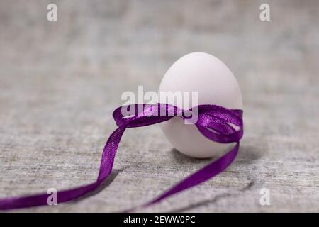 œuf de poulet emballé dans un nœud papillon violet. nourriture saine et crue. œuf de pâques, présent. Banque D'Images