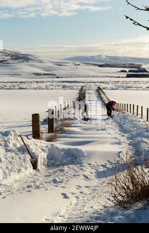 Mère et fille qui pelent de la neige de l'allée, Orkney Isles Banque D'Images