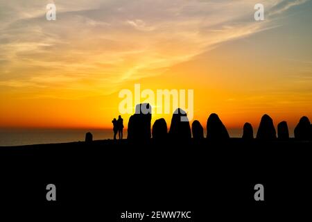 Ciel partiellement nuageux et coloré au coucher du soleil sur la mer. Silhouettes d'Ales Stenar, monument mégalithique de Kaseberga, Scania, Suède, février 2021. Banque D'Images