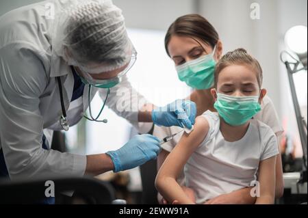 Un pédiatre expérimenté vaccine une petite fille, la mère tient le bébé dans ses bras, la fille a peur Banque D'Images