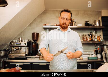 Homme avec un couteau à aiguiser la barbe et la moustache, travaillant au restaurant Banque D'Images