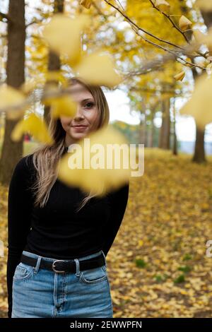 Une jeune femme blonde se tient sous une verrière de gingko arbres à l'automne Banque D'Images