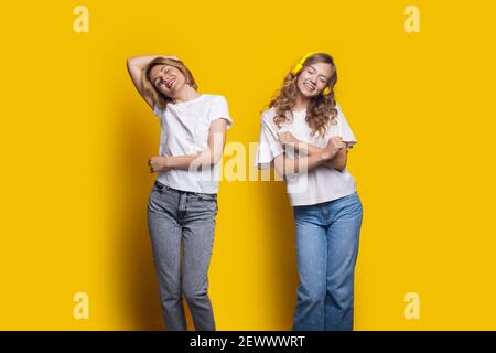 Deux sœurs applaudissent écoutent de la musique à l'aide de casques et danse sur un mur jaune de studio Banque D'Images