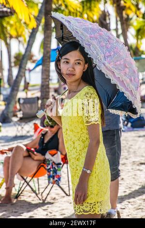 Une jeune femme avec parasol se trouve sur la plage de la piscine de l'atoll au parc Matheson Hammock à Miami, en Floride. Banque D'Images