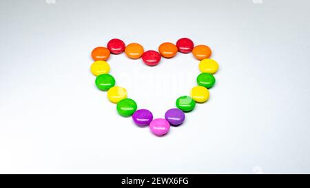 Mise au point sélective de chocolats colorés disposés en forme de coeur sur fond de papier blanc. Banque D'Images