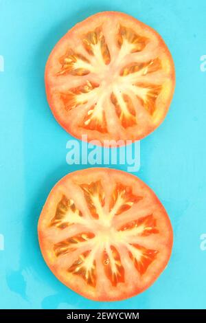 Gros plan de deux tranches de tomates rouges rondes sur fond bleu, ambiance d'été fraîche. Photo vierge pour votre modèle, orientation verticale rectangulaire. Banque D'Images