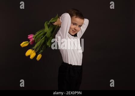 le garçon avec le vitiligo dans une chemise blanche et un Noeud papillon avec tulipes sur fond noir Studio Banque D'Images