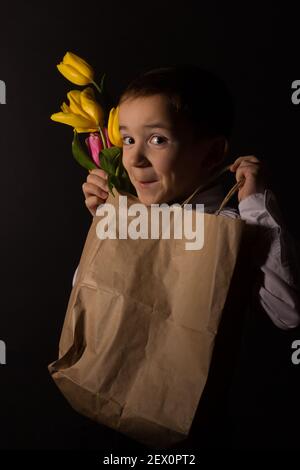 le garçon avec le vitiligo dans une chemise blanche et un Noeud papillon avec tulipes sur fond noir Studio Banque D'Images