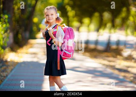 Belle petite fille avec sac à dos randonnée pédestre dans le parc prêt de nouveau à l'école, l'automne à l'extérieur, de l'éducation concept. Banque D'Images