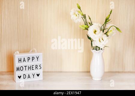 Boîte lumineuse avec lettrage Happy Mother's Day, fleurs blanches Eustoma ou Lisianthus dans un vase sur fond de bois avec espace de copie. Banque D'Images