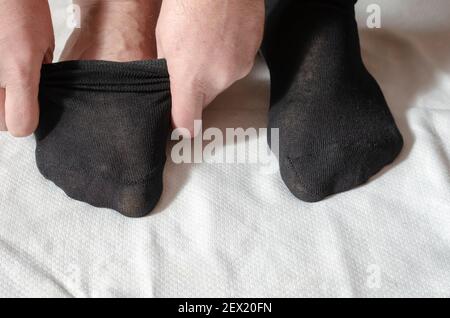 Les mains d'un homme adulte mettent de nouvelles chaussettes. Un homme à la maison le matin met des chaussettes grises sur sa jambe. Cliquez. Mise au point sélective Banque D'Images