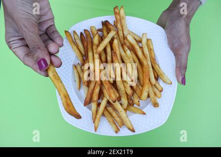 Femelle tenant une assiette de croquant croquant croquant frites tas. Pommes de terre au doigt avec masala. Très savoureux encas populaire à l'heure du thé dans le monde entier Banque D'Images