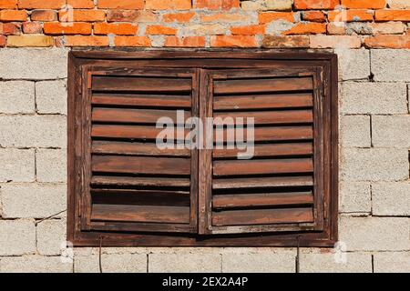 Vieux mur de bâtiment en brique avec fenêtre couverte de stores en bois fermés, cassés et abîmés Banque D'Images