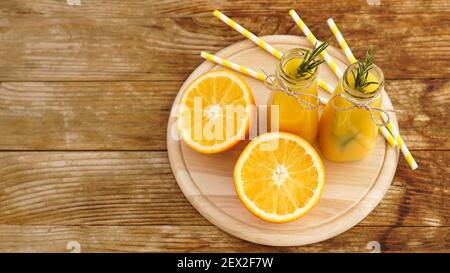 Jus d'orange en bouteilles de verre. Le jus est décoré d'une branche de romarin. Jus sur fond en bois Banque D'Images