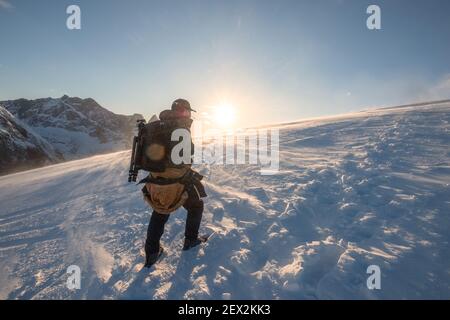 Randonnée Mountaineer sur la colline de neige jusqu'à la montagne supérieure avec la lumière du soleil briller au coucher du soleil. Mont Ryten, îles Lofoten Banque D'Images