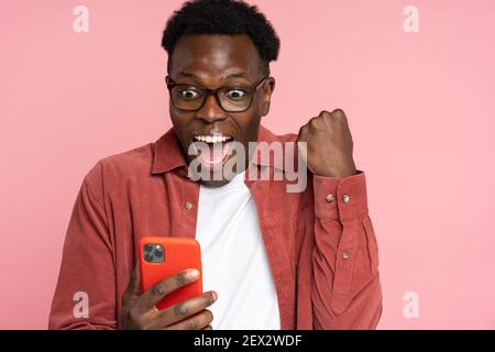 Un homme noir plein de joie regarde le smartphone, le sourire se sent heureux de lire les bonnes nouvelles, faisant le geste du gagnant Banque D'Images