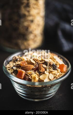 Petit déjeuner céréales dans le bol. Muesli sain avec flocons d'avoine, noix et raisins secs sur table noire. Banque D'Images