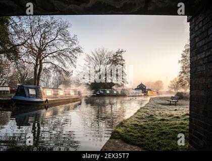 Magnifique ancienne maison de canal bateaux paysage sous le pont lever du soleil dans la campagne avec rivière et un seul banc en bois solitaire. Givre sur les arbres de réflexion de l'herbe Banque D'Images