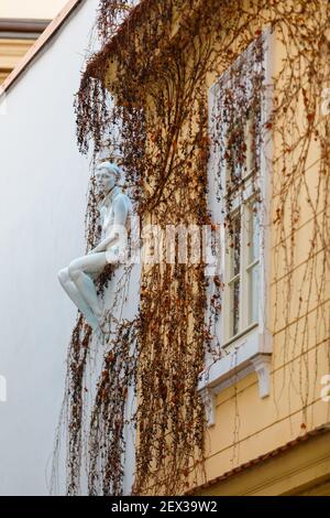 Prague, République tchèque le 14 avril 2018. Sculpture d'une fille assise sur le bord du toit du bâtiment. Les plantes poussent sur le mur. Banque D'Images
