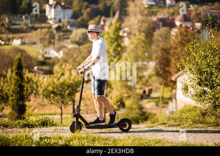 Jeune homme en tenue décontractée sur un scooter électrique de coup de pied rue de la ville en été Banque D'Images