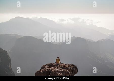 L'homme s'assoit au bord du grand rocher entouré par magnifique paysage de montagne Banque D'Images