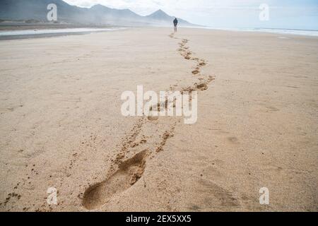 Empreintes de pieds sur une plage de sable. Un homme solitaire longe la plage en laissant des empreintes de pas sur le sable Banque D'Images