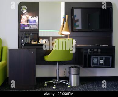 Un endroit moderne pour travailler et faire des affaires dans la chambre d'hôtel, avec une table, chaise verte, lampe moderne, tv, coffre-fort, machine à café Banque D'Images