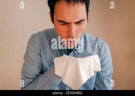 Guy tousse. Éternuez dans un chiffon. Un jeune caucasien attrayant tousse intensivement et couvre sa bouche avec une serviette. Rhume, grippe, mal de gorge, respira aiguë Banque D'Images
