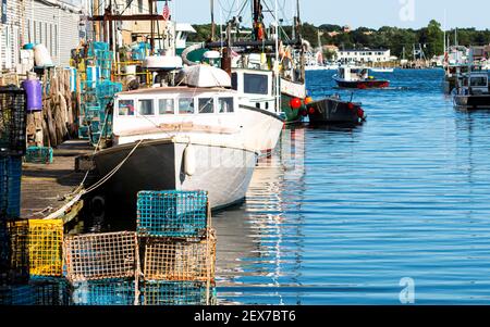 Bateaux de pêche au homard amarrés derrière les magasins dans un canal de Porland Maine avec des casiers à homard et des outils de pêche empilés sur le quai. Banque D'Images