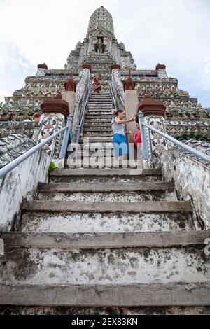 Touristes utilisant les marches pour grimper au sommet de la flèche à l'intérieur du complexe du temple de Wat Arun à Bangkok. Banque D'Images