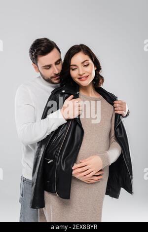 Homme portant une veste sur une femme enceinte souriante isolée sur le gris Banque D'Images