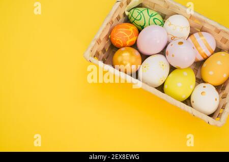 Un panier tissé rempli d'œufs de Pâques colorés sur jaune arrière-plan Banque D'Images