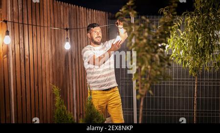 Faites la fête dans l'arrière-cour avec un homme heureux qui pendait des guirlandes de lumières dans les arbres Banque D'Images