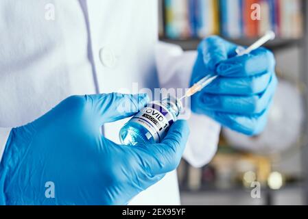 gros plan d'un professionnel de la santé, portant un manteau blanc et des gants chirurgicaux bleus, remplissant une seringue d'un flacon simulé de vaccin covid-19, dans un hou Banque D'Images