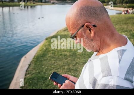 homme de 65 ans regardant son smartphone dans un parc Banque D'Images