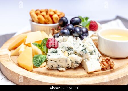 Planche avec différents types de fromage. Mélange de fromages dor bleu chedar parmesan brie sauce miel pain aux doigts et raisin sur patte de laine. Menu restaurant plaque petit déjeuner. Assortiment de collations santé Banque D'Images