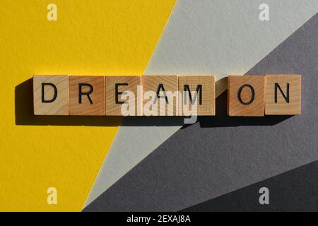 Dream On, des mots en lettres de l'alphabet en bois isolés sur fond jaune et gris Banque D'Images