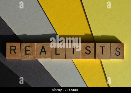 Réalistes, mot en lettres de l'alphabet de bois isolées sur fond jaune et gris Banque D'Images