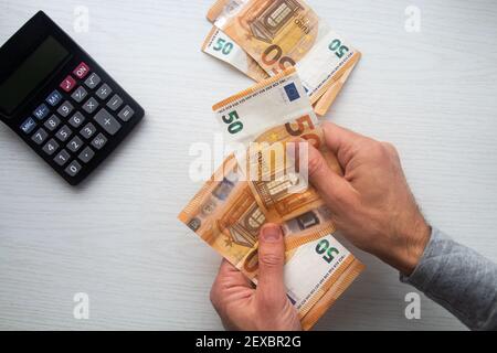 Homme remet en main le comptage des billets de banque en euros et la calculatrice table blanche Banque D'Images